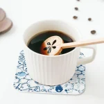 White mug on science-themed coaster with wooden spoon.
