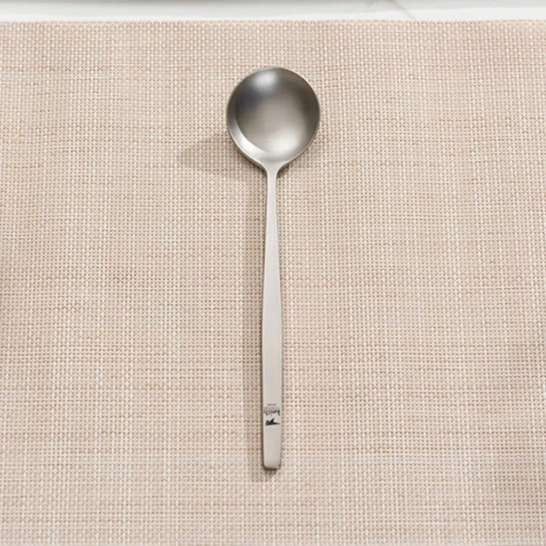 Stainless steel soup spoon on woven placemat.